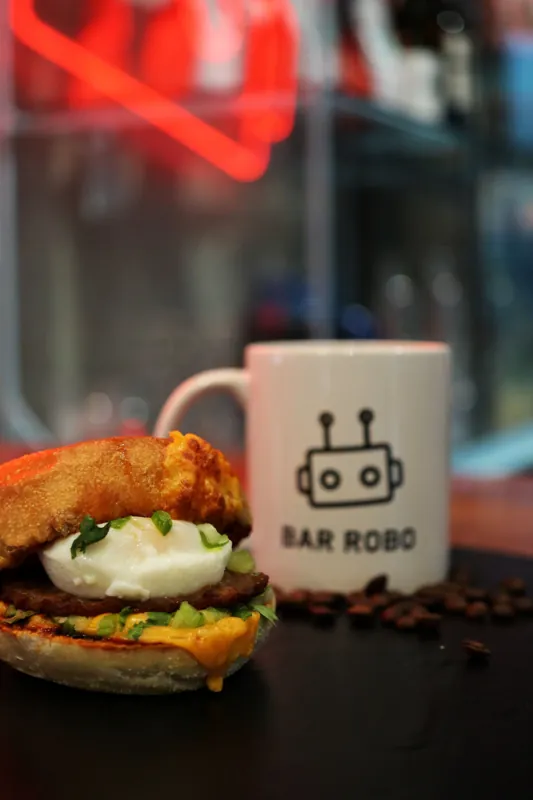 A breakfast sandwich beside a white Bar Robo coffee mug.