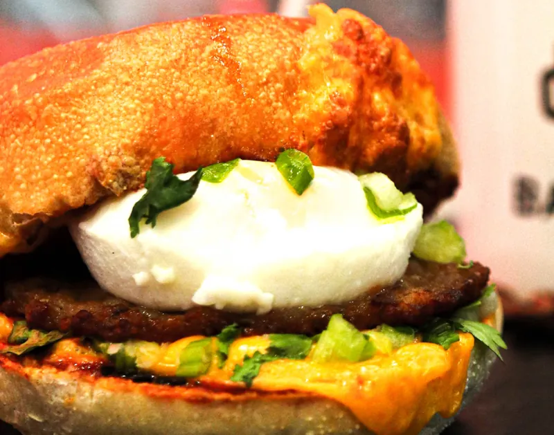 A breakfast sandwich with egg, greens and melted cheese on a toasted bun.
