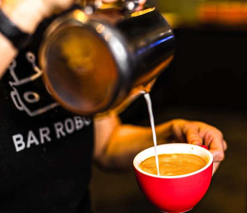 A Bar Robo barista pouring coffee into a red cup.