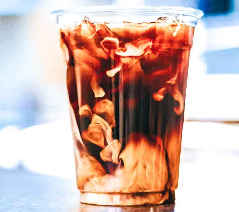 Milk swirling into a glass of iced coffee.