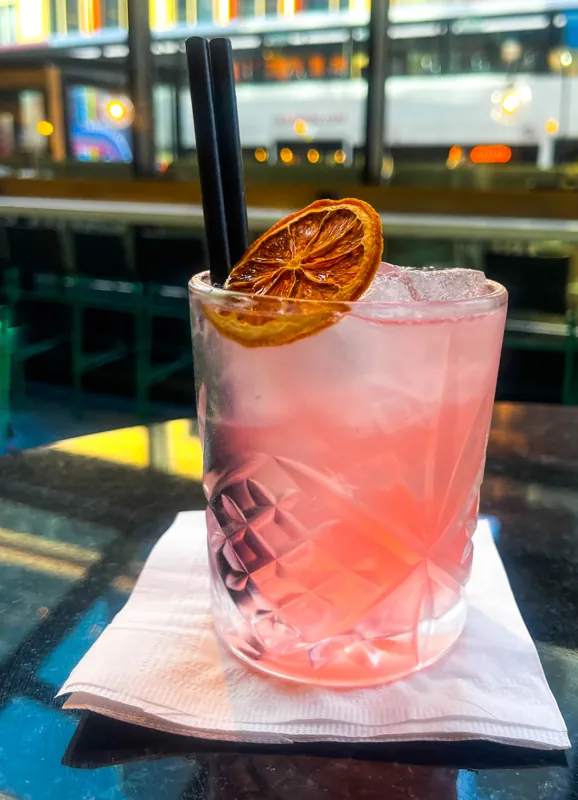A pink cocktail topped with a dried citrus slice.